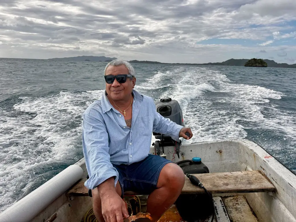 Man steering an open longboat across the water toward Lomaloma, Vanua Balavu, Fiji